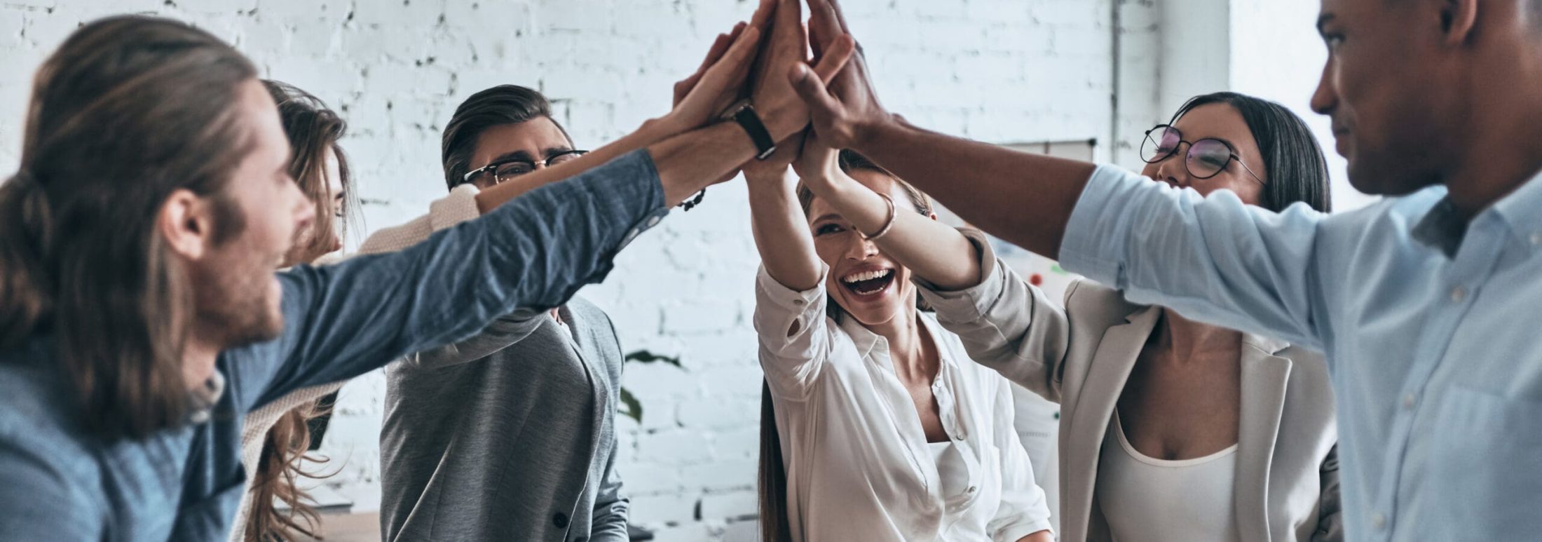 High-five for success! Diverse group of business colleagues giving each other high-five in a symbol of unity and smiling while working in the board room